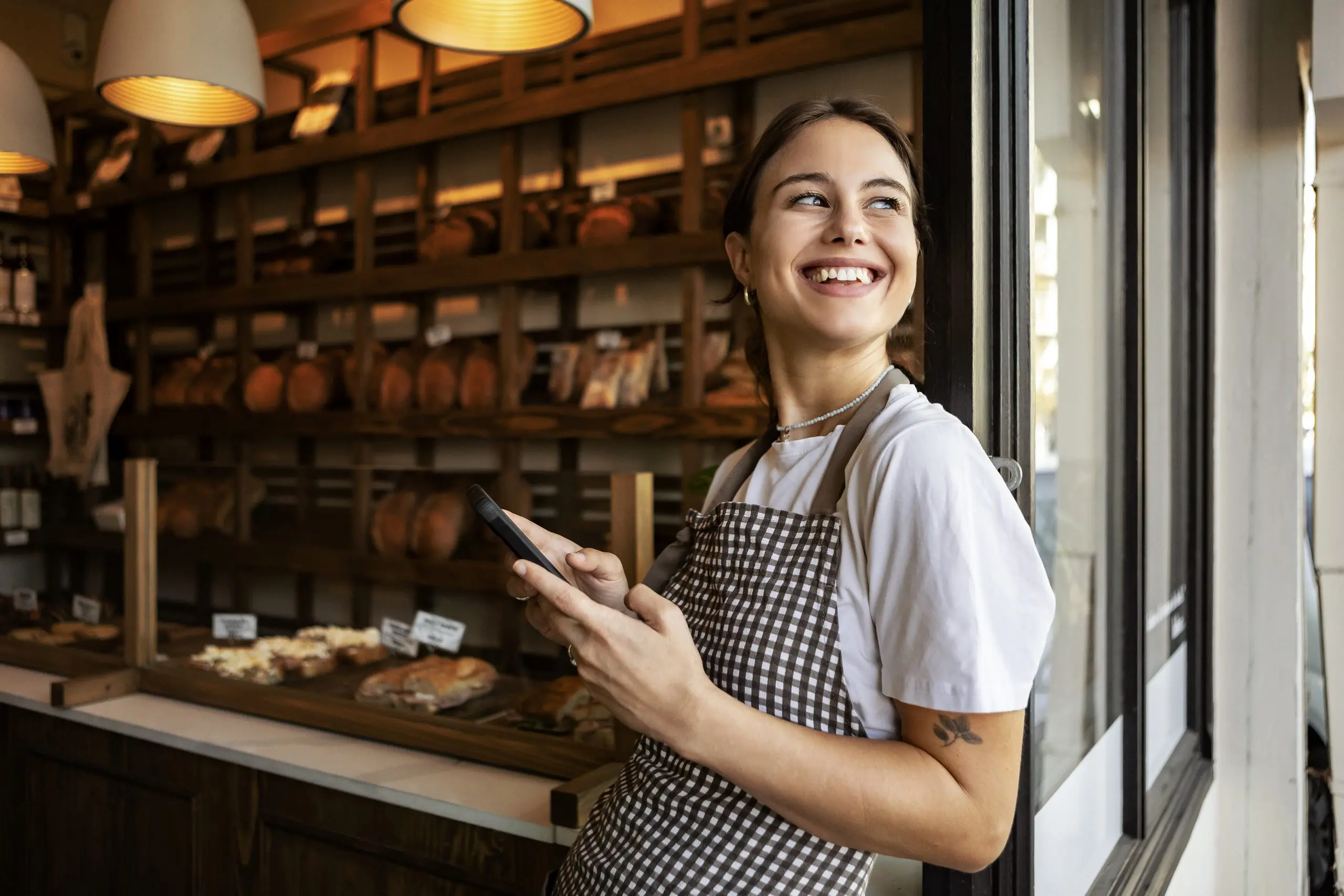 Baker standing proudly in front of her bakery using her phone